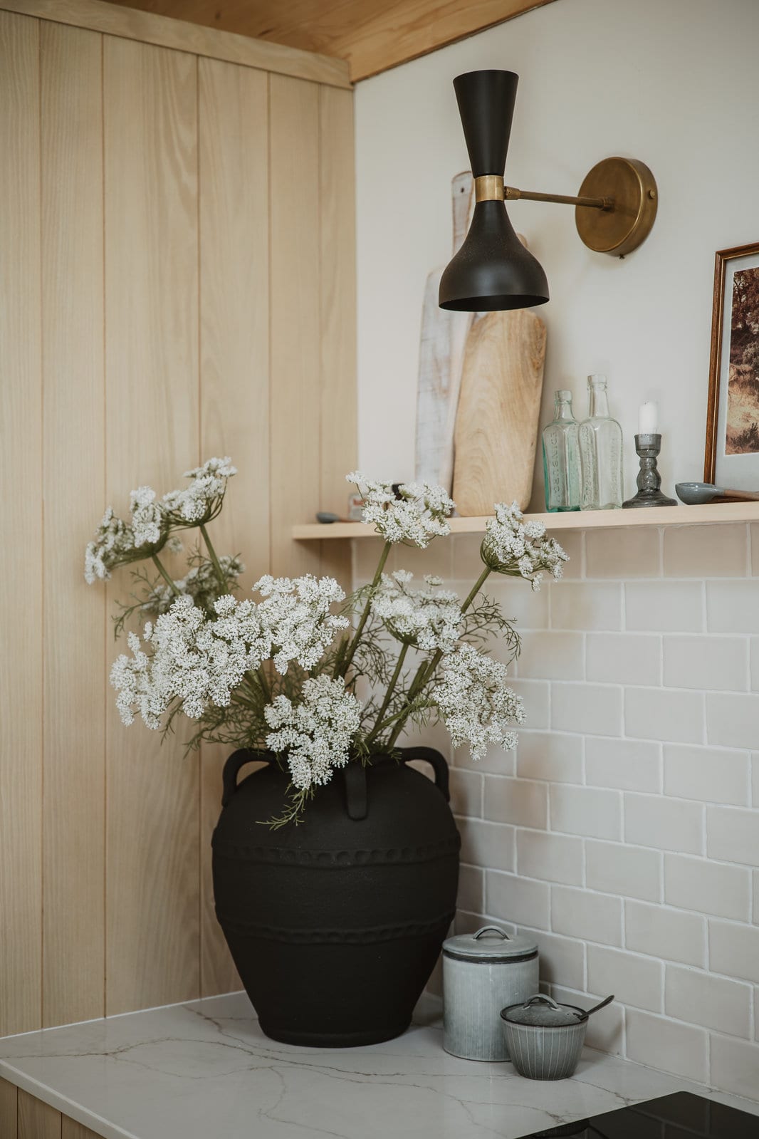Ebony & Ivory: white umbel flowers in a black textured urn on a marble worktop, against pale timber and white tiles.