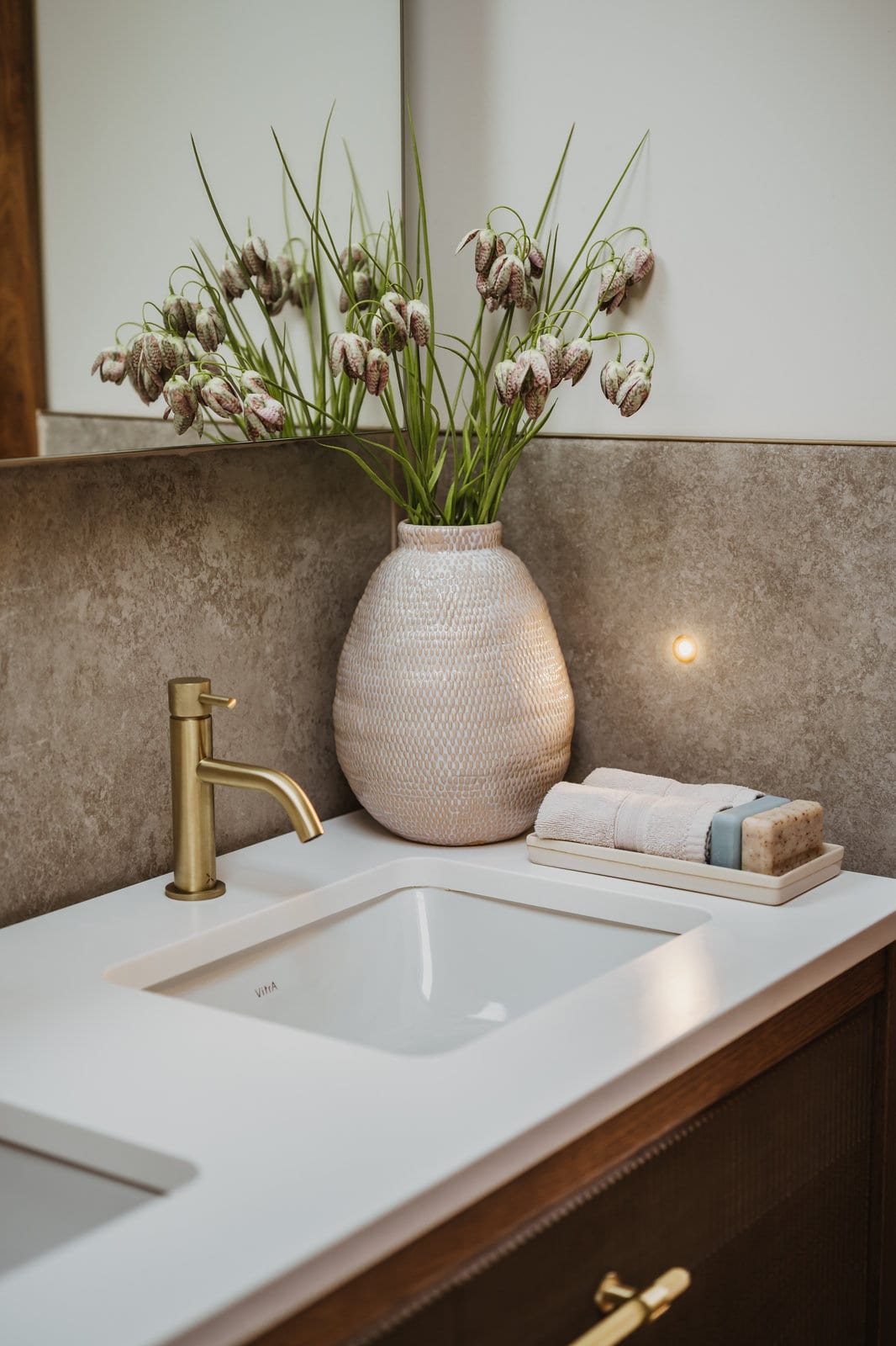 Meadow Bells: checked fritillary heads on tall grassy stems in a textured cream vase, on a bathroom vanity with brass taps.