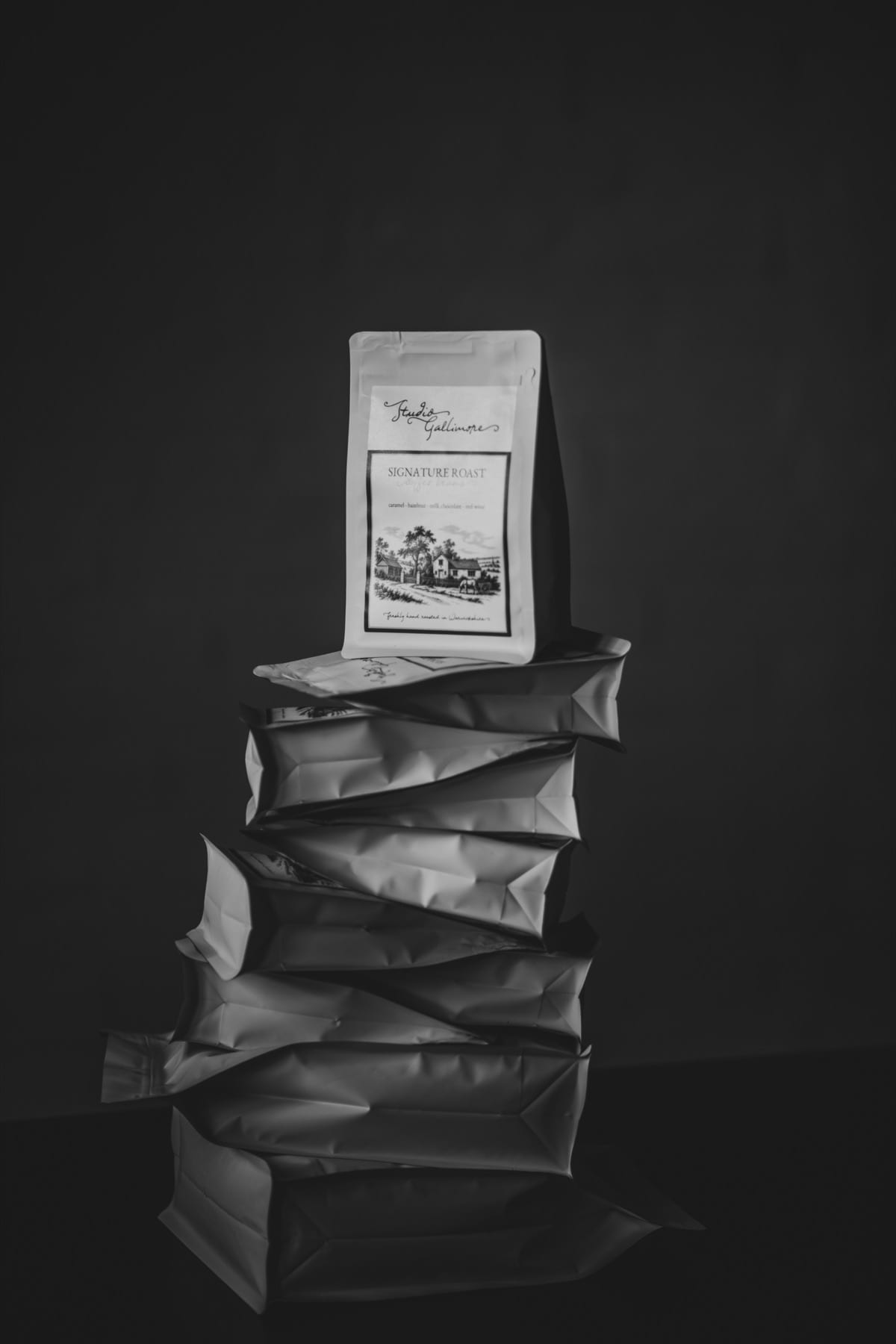 Seven bags of Studio Gallimore Signature Roast stacked one on another against a dark ground, the topmost standing upright.