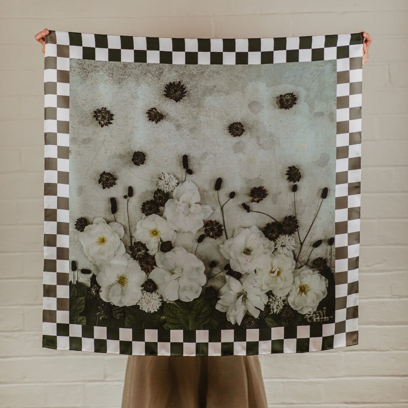 Belle, a silk scarf printed with white garden roses and scabiosa beneath dark astrantia and sanguisorba heads on a pale ground, framed by a brown and white checkerboard border.