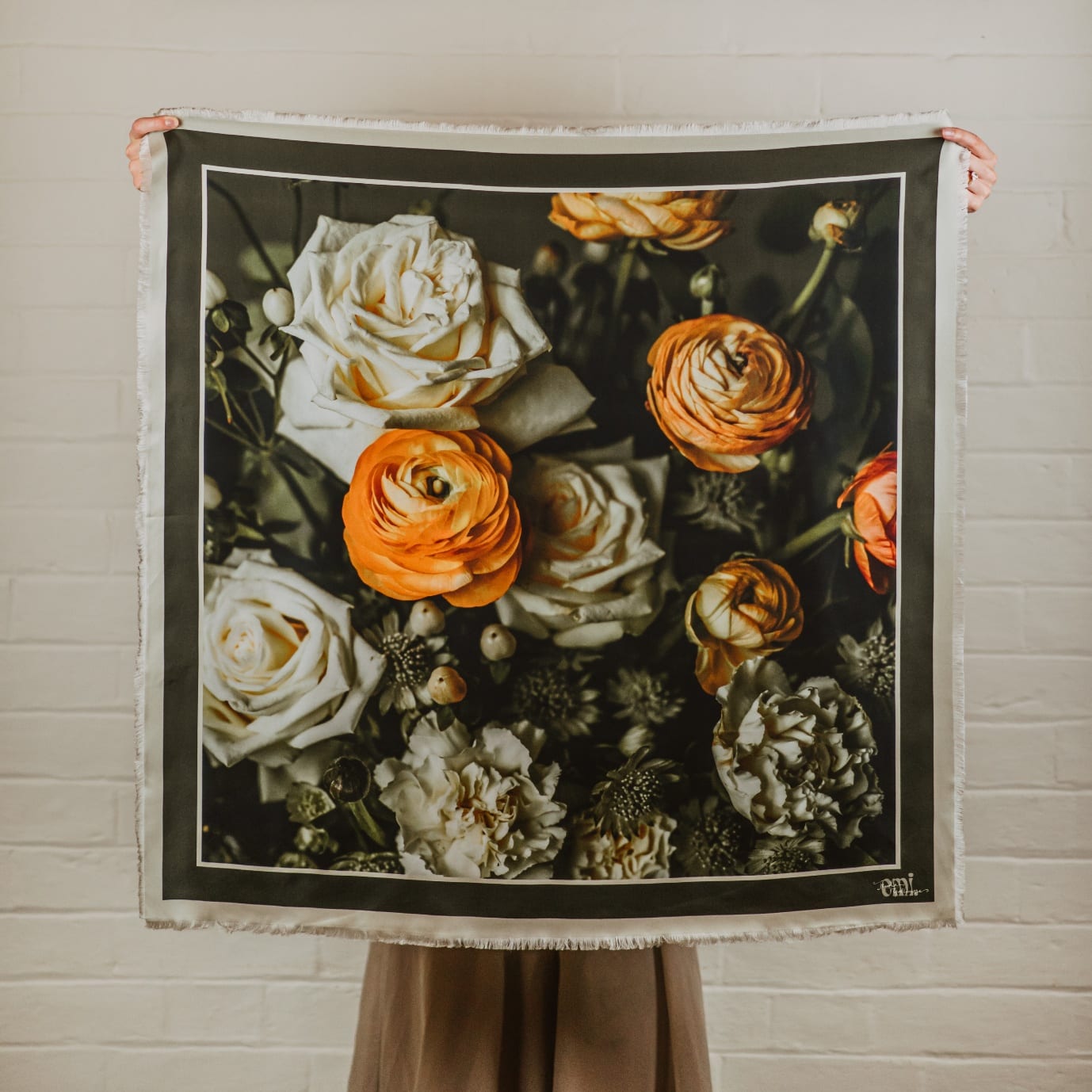 Betsy, a silk scarf printed with orange ranunculus and cream roses against a dark ground, with a soft beige frayed edge.