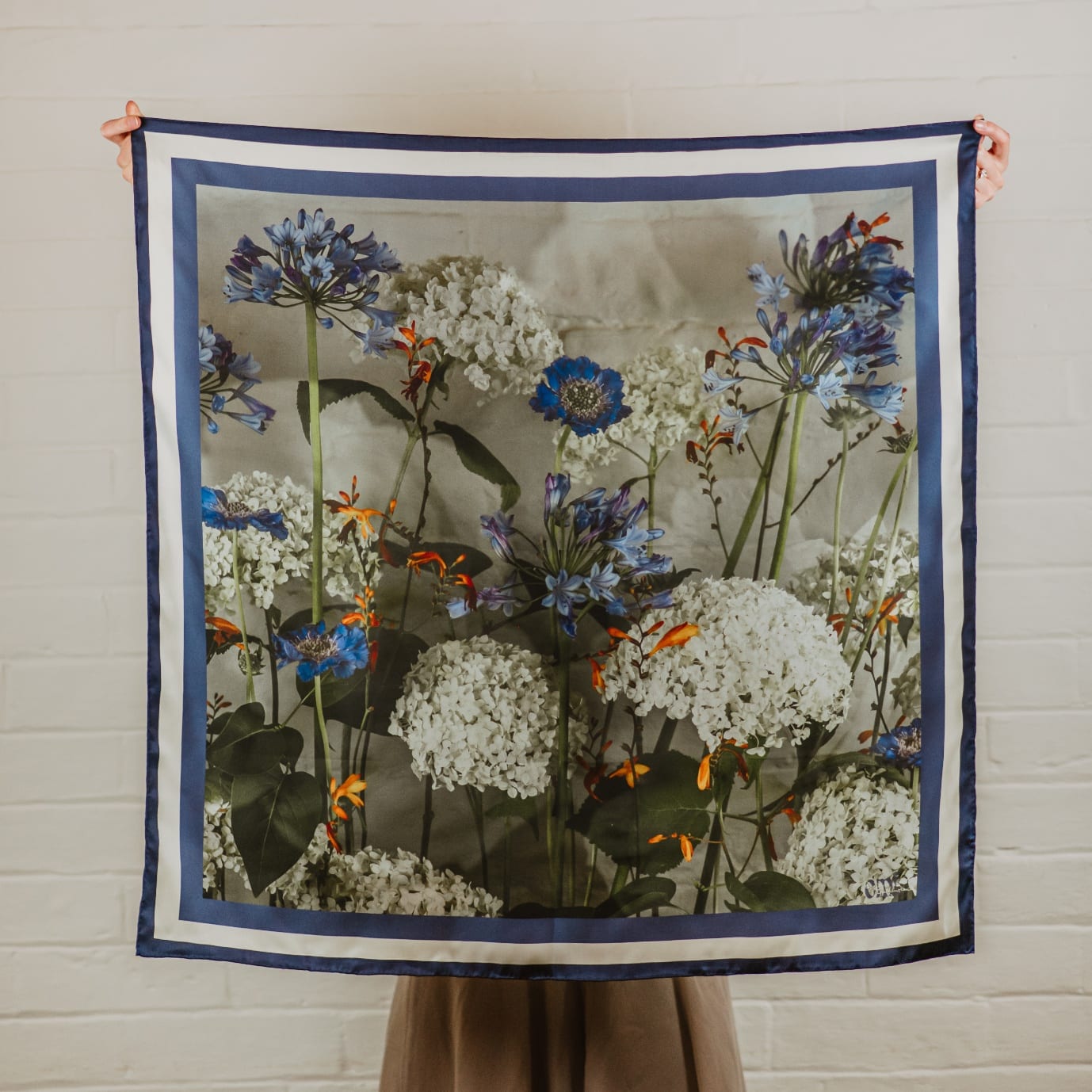 Blu, a silk scarf printed with blue agapanthus, ivory hydrangeas and orange crocosmia on a soft grey ground, framed in navy and cream stripes.