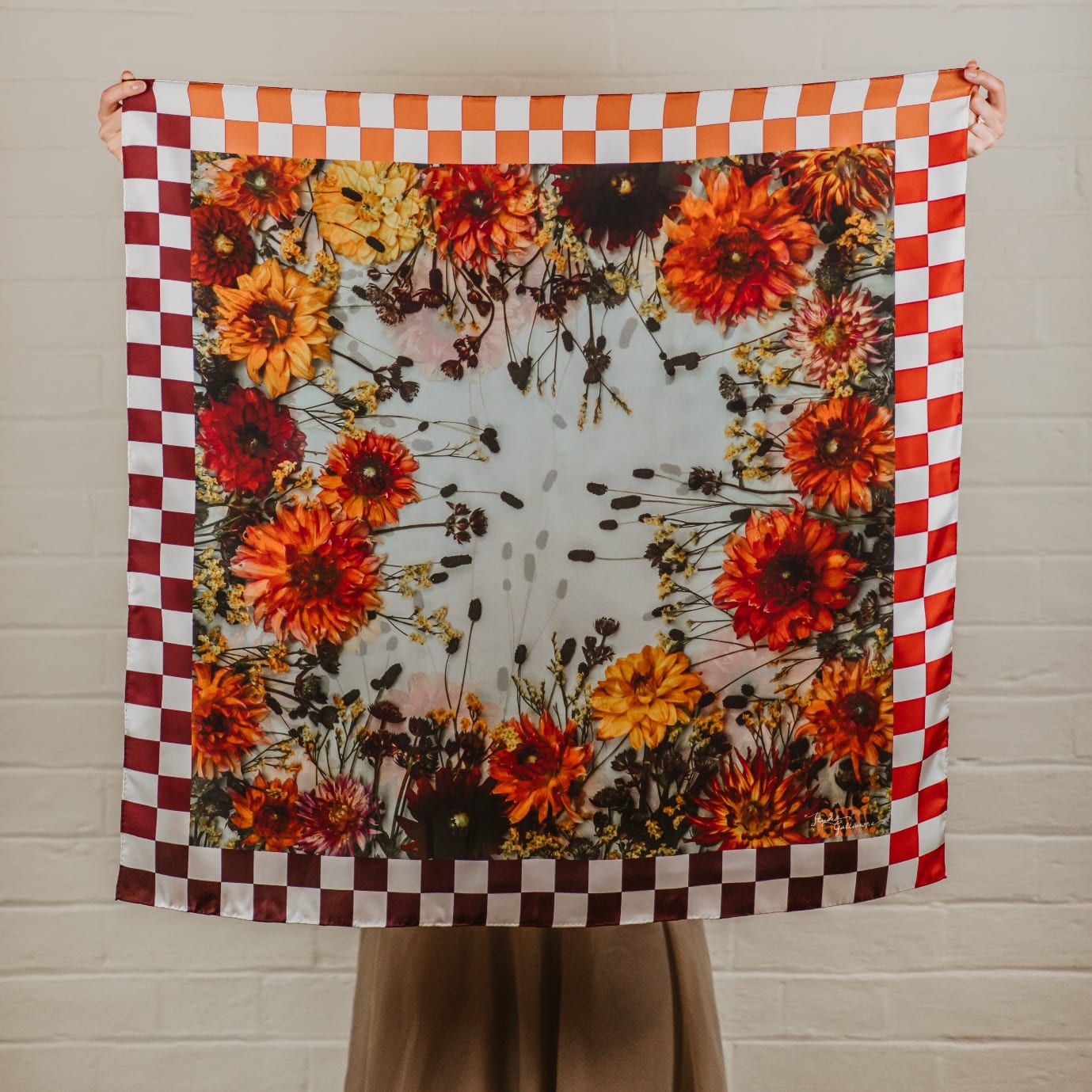 Blythe, a silk scarf printed with a ring of orange, red and gold dahlias on a pale ground, inside an orange and red check border.