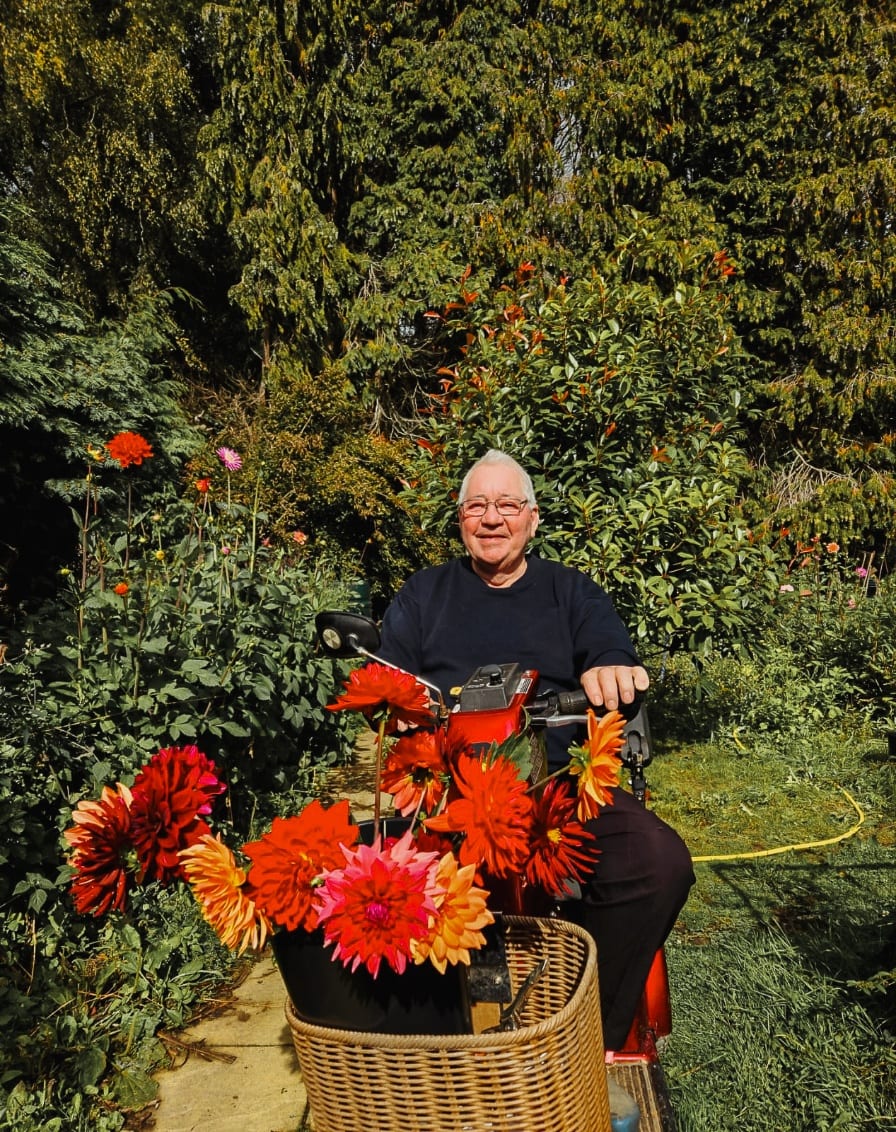 Mr H seated in his garden with a wicker basket full of red and orange dahlias.